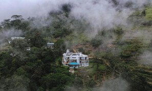 A large, multi-story building surrounded by dense forest, with a visible swimming pool and a clear view of the surrounding landscape. - Villa Vajrapani (Kandy)