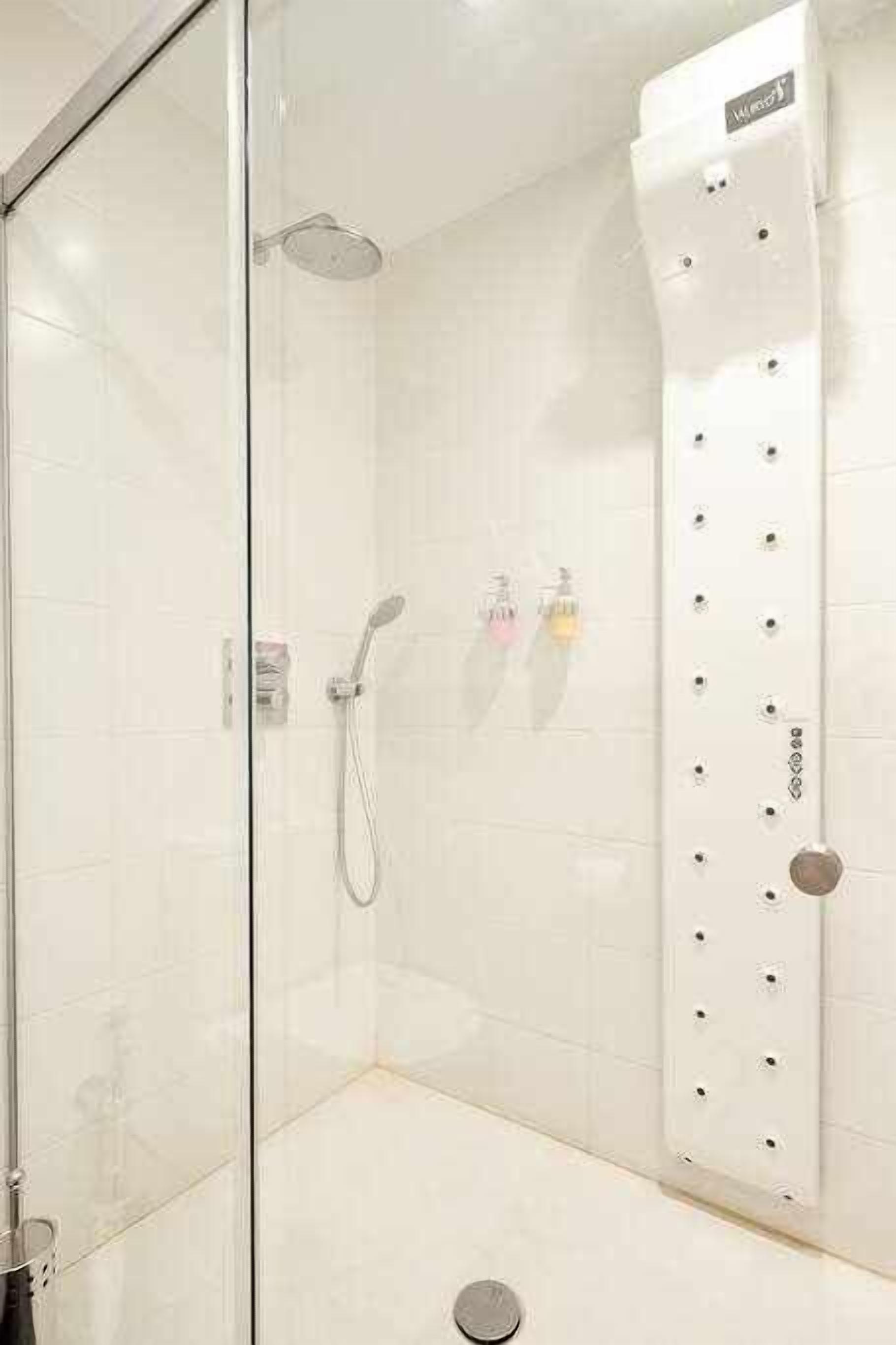 Une douche fermée par des parois en verre, dotée d’un pommeau de douche à main et d’un panneau de commande fixé au mur.