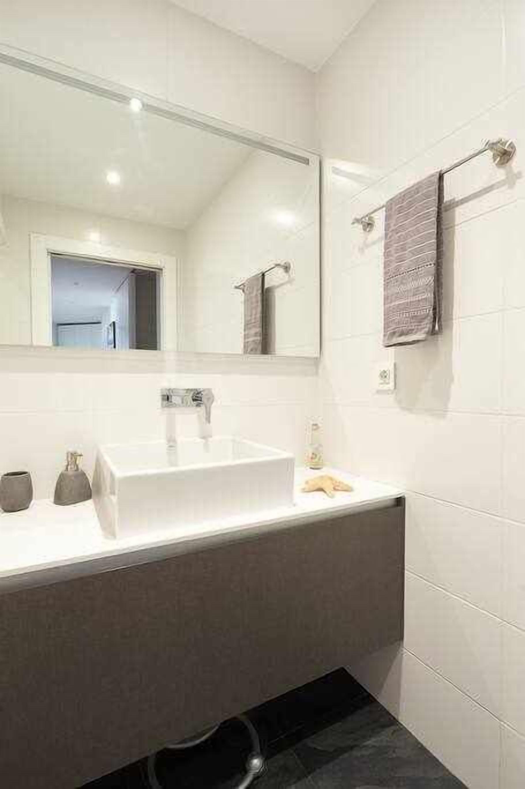 A modern bathroom with a large mirror, a white sink, and a towel rack.