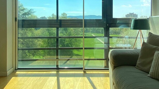Una habitación con amplios ventanales, suelo de madera y sofá verde.