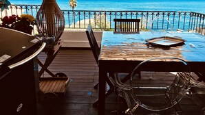 Un espacio de comedor al aire libre con techo y vistas al mar, una parrilla y una mesa con sillas.