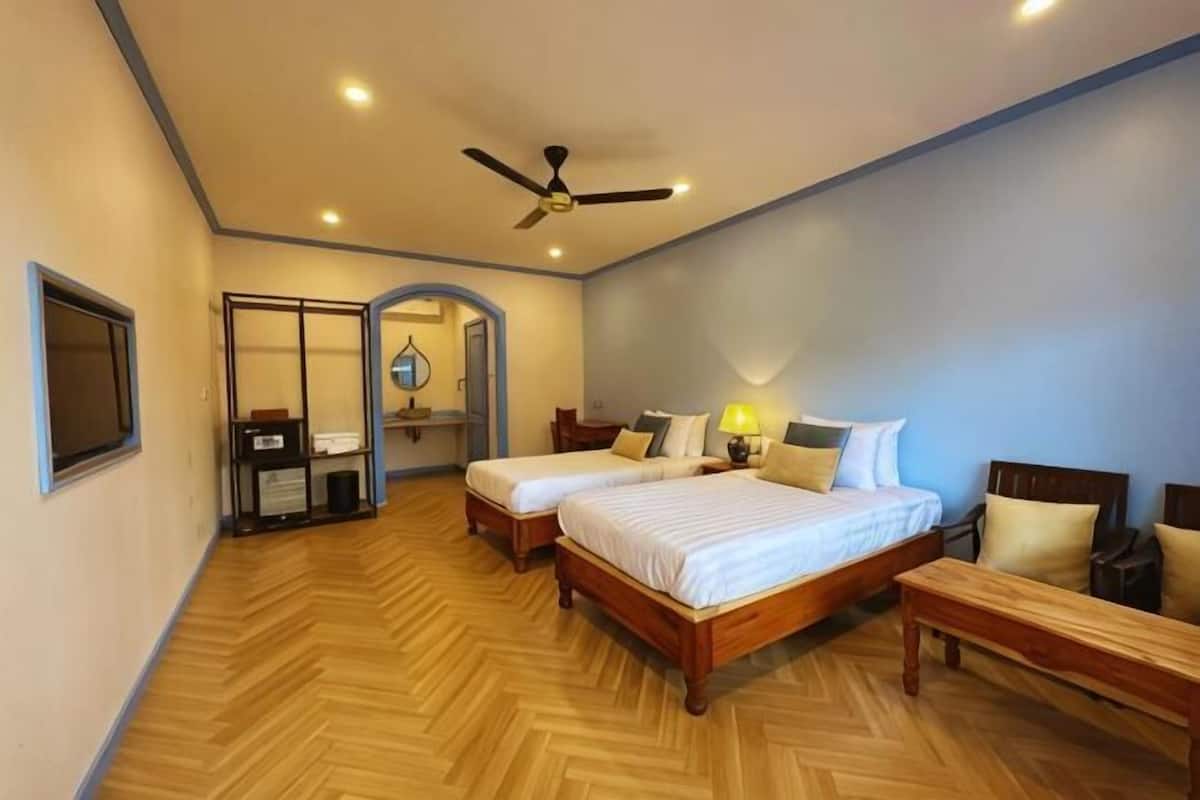 A hotel room with two beds, a ceiling fan, a wooden floor, a desk, and a mirror.