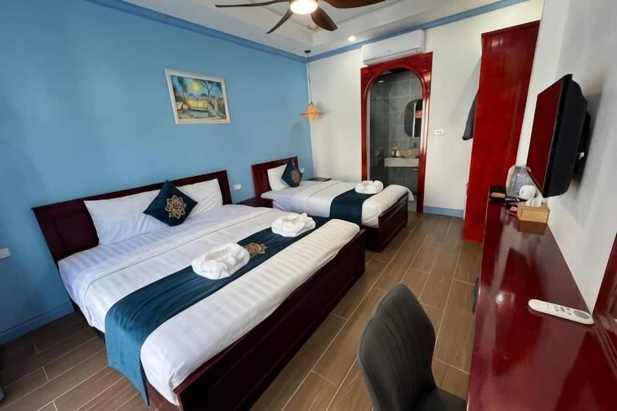A hotel room with two beds, a desk, a chair, a ceiling fan, and a red door.