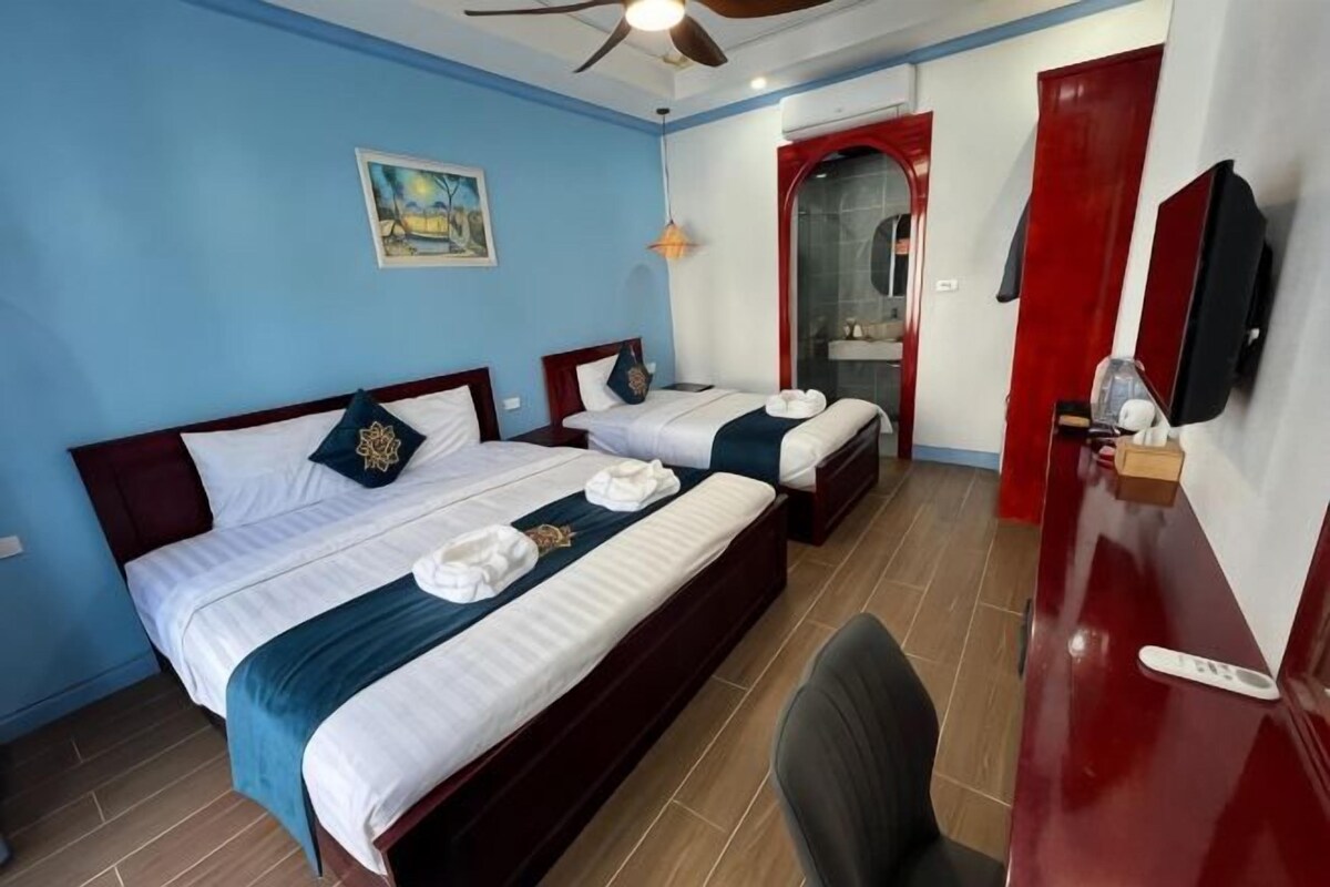A hotel room with two beds, a desk, a chair, a ceiling fan, and a red door.