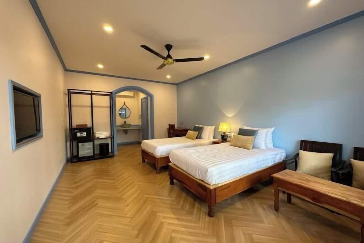 A hotel room with two beds, a ceiling fan, a wooden bench, and a wardrobe with a mirror.