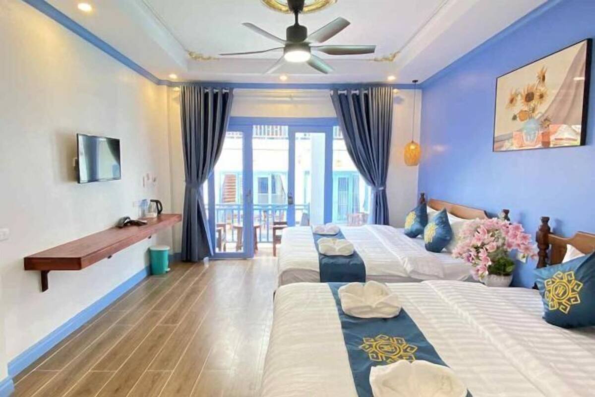 A hotel room with two beds, a TV, a ceiling fan, and a view of the outside.