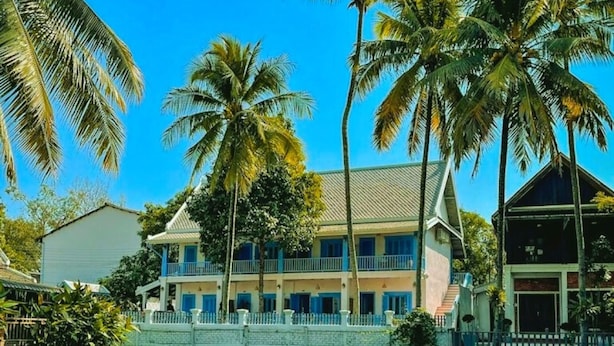 A hotel with a large building, palm trees, and a pond with pink water lilies. - Sadakham hotel (Luang Prabang)