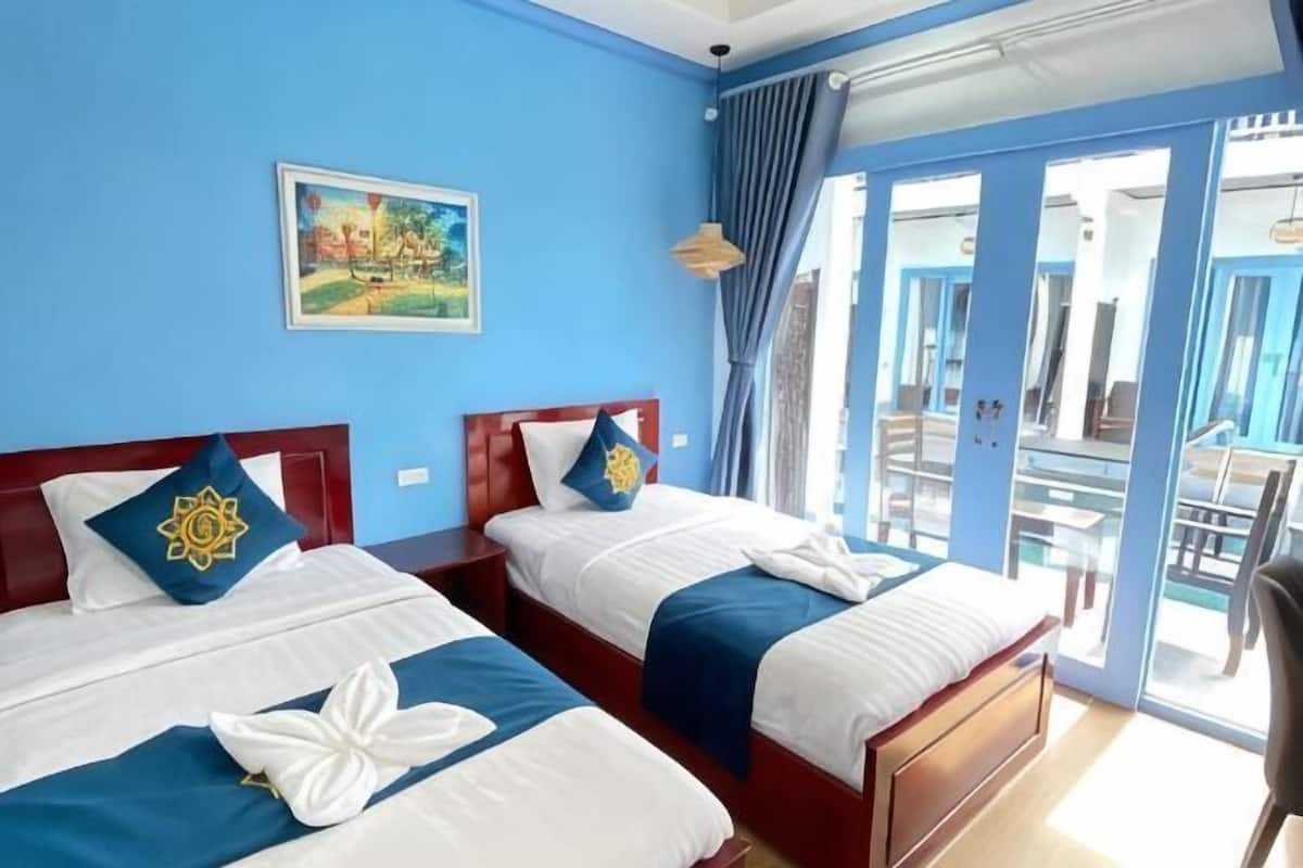 A hotel room with two beds, a painting on the wall, and a view through the glass door.