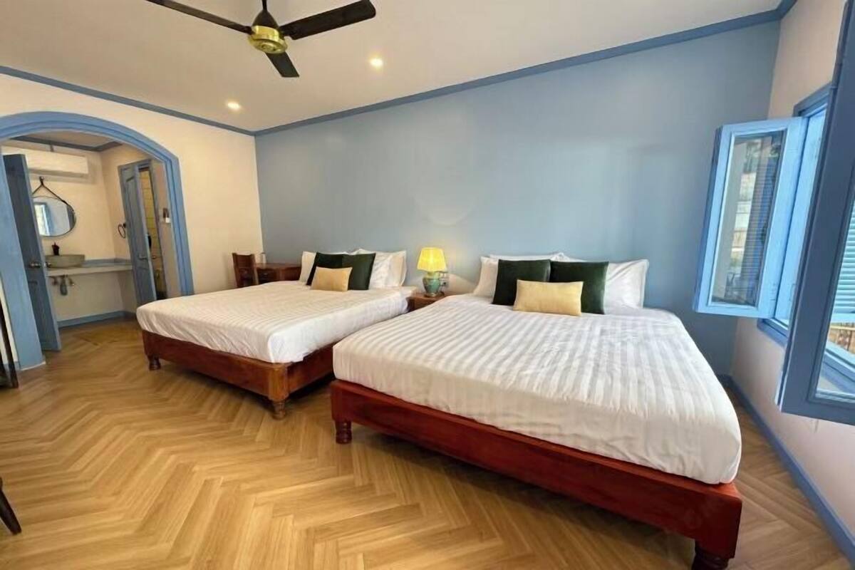 A room with two beds, a ceiling fan, and a window with blinds.