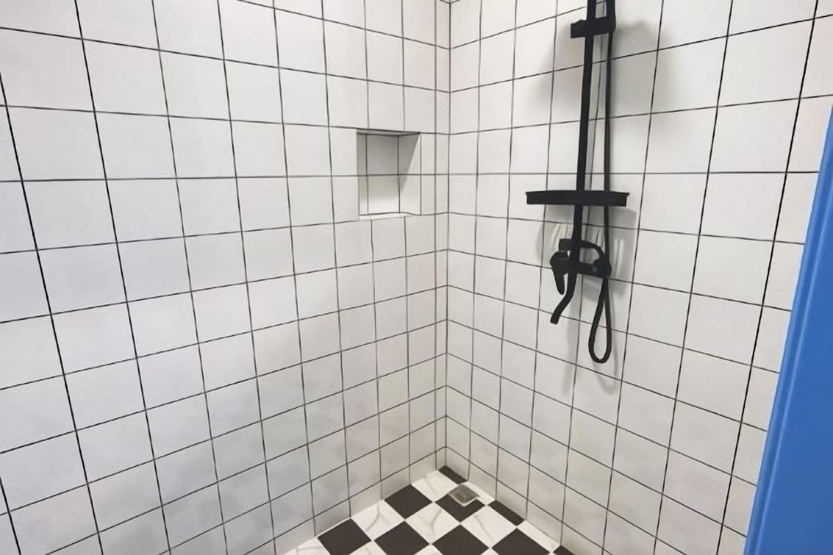 A tiled shower area with a checkered floor, a black showerhead, and a small shelf.