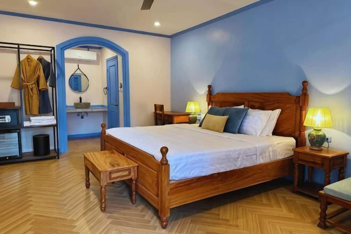 A bedroom with a wooden bed, bedside tables, a bench, a wardrobe, and a mirror.