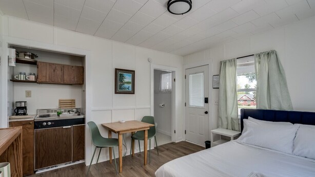 Une pièce compacte comprenant un lit, une petite kitchenette, un coin repas et une fenêtre avec des rideaux.