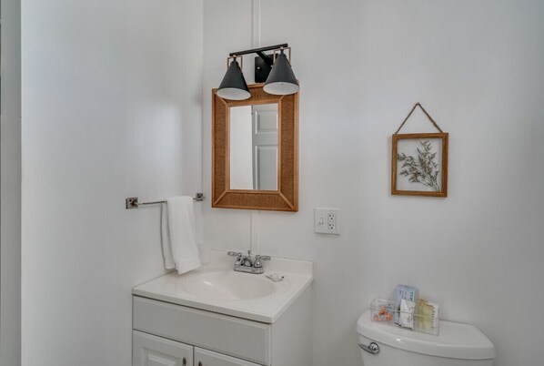 Ein Badezimmer mit einem weißen Waschbecken, einem Spiegel mit Holzrahmen und einem gerahmten Bild an der Wand.