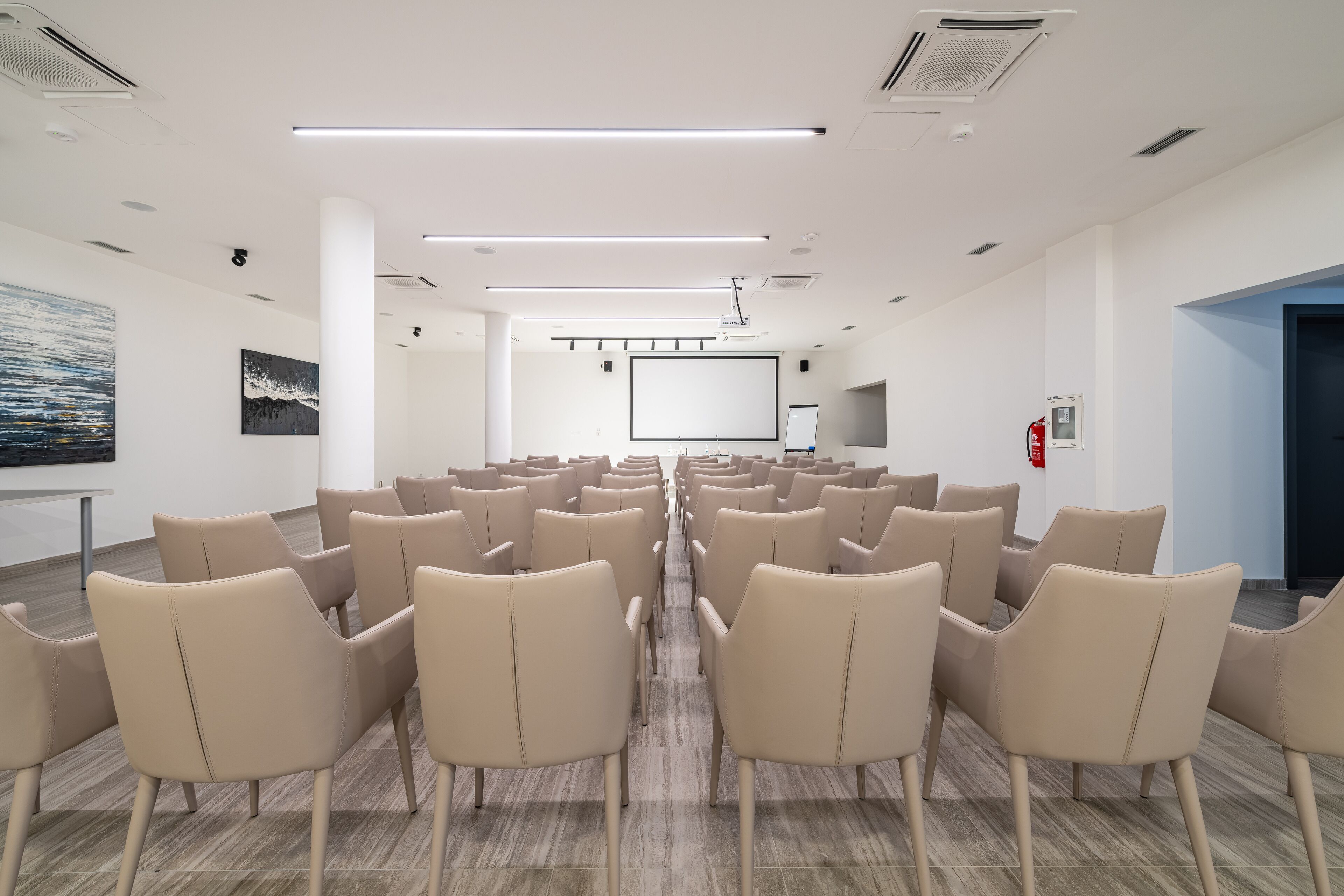 A conference room with rows of beige chairs, a projector screen, and a whiteboard.