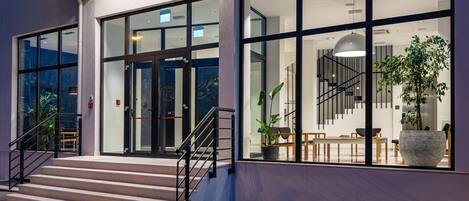 Una entrada de hotel moderna con fachada de vidrio, una escalera que conduce a la entrada y una planta grande en maceta cerca de la entrada.