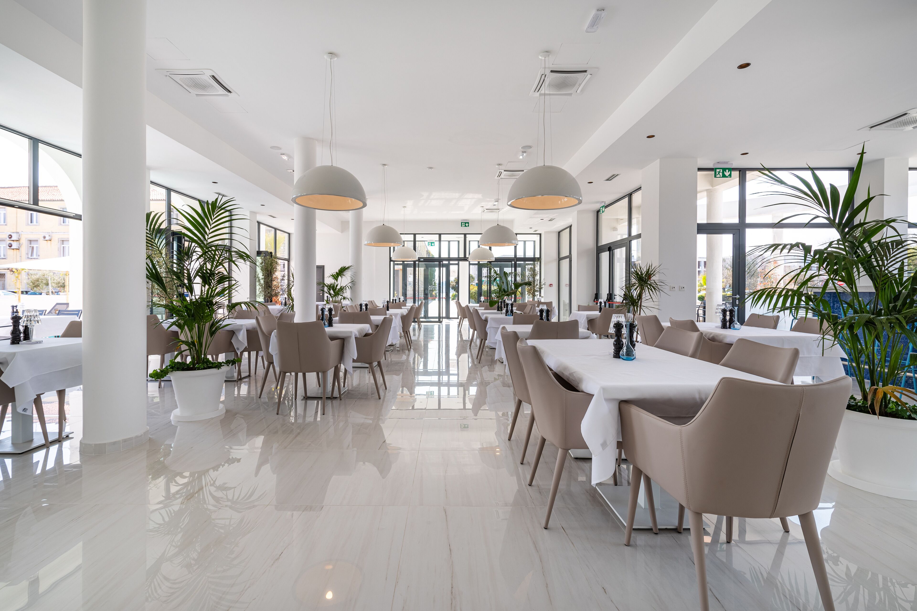 Un amplio comedor interior con varias mesas y sillas, ventanas grandes y plantas en macetas.