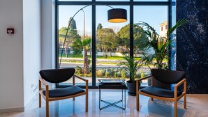 A modern waiting area with two black chairs, a table, and a large window offering a view of a park and buildings. - Miramare Hotel Zadar (Zadar)