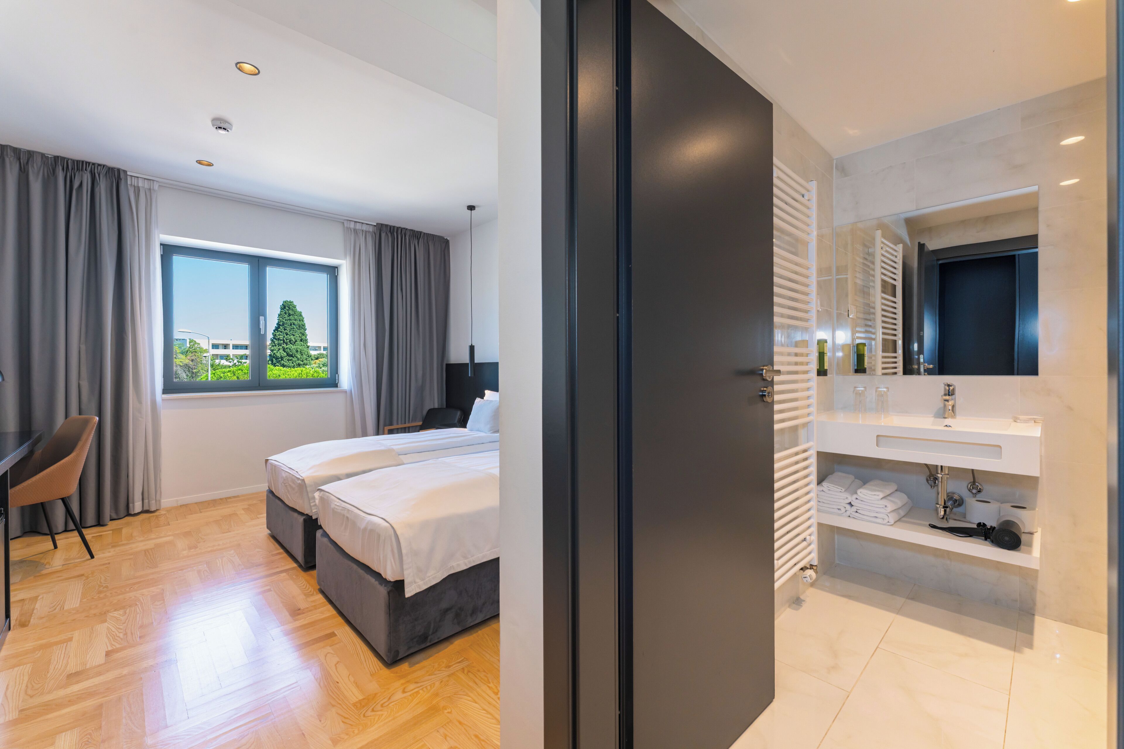 A modern hotel room with a bed, a desk, and a bathroom with a mirror and sink.