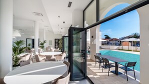 A modern outdoor dining area with a pool view, featuring glass doors, white furniture, and a clear sky. - Miramare Hotel Zadar (Zadar)
