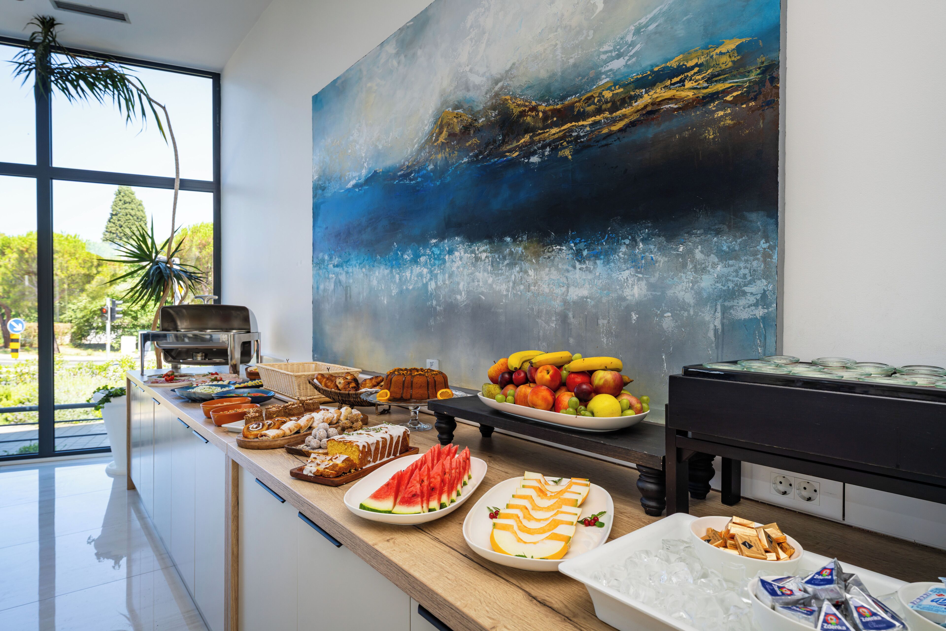 Une table de buffet garnie de divers plats et, au mur, un grand tableau abstrait.