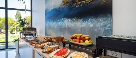 A buffet table with various food items and a large abstract painting on the wall.