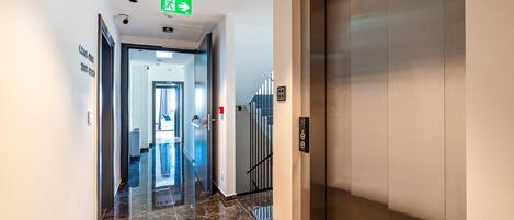 A modern hotel corridor with a polished marble floor, an elevator, and a staircase leading to another floor.