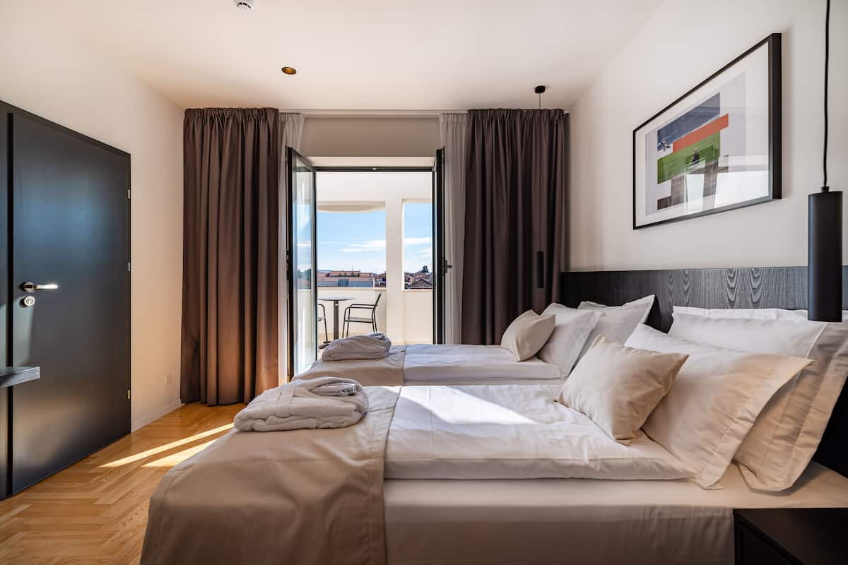 A hotel room with two beds, a view to the outside, and a framed picture on the wall.