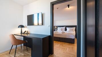 Una habitación de hotel moderna con suelo de madera, un escritorio con silla, una cama con ropa blanca y un espejo grande.