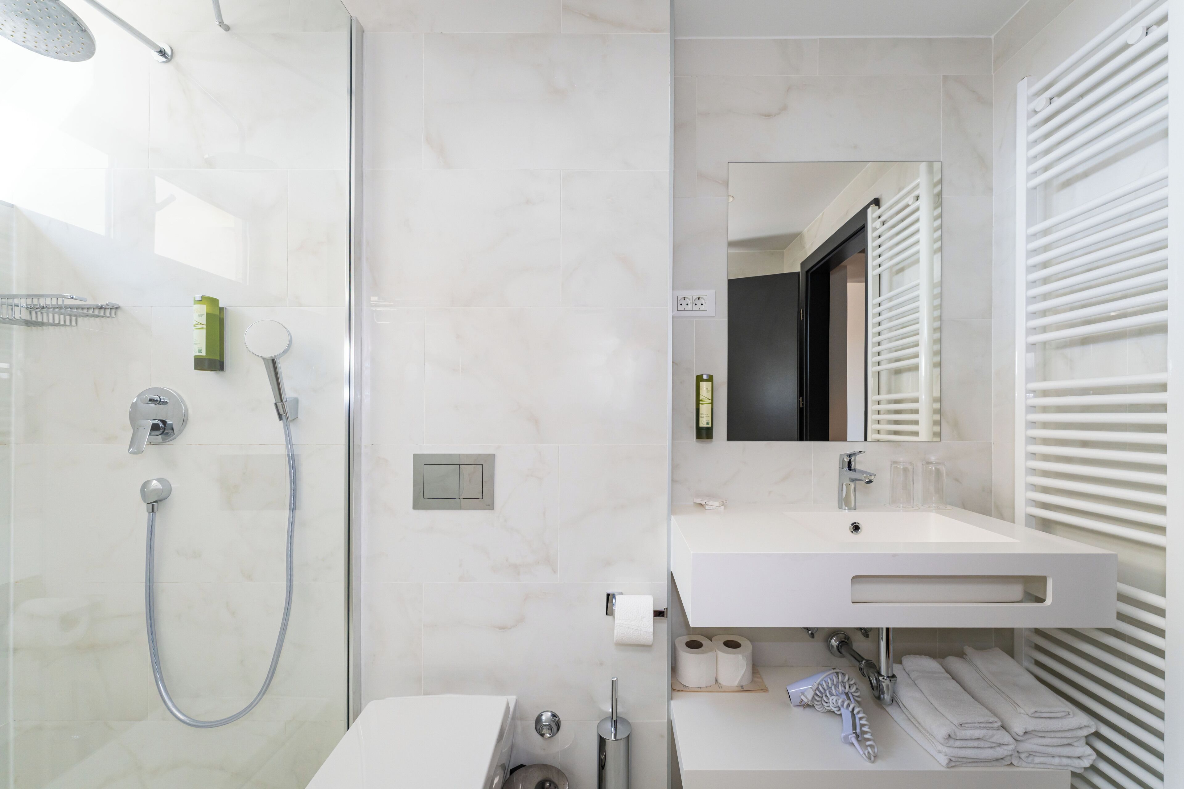 Un baño moderno con cabina de ducha de vidrio, un lavabo blanco con espejo y un perchero para toallas.