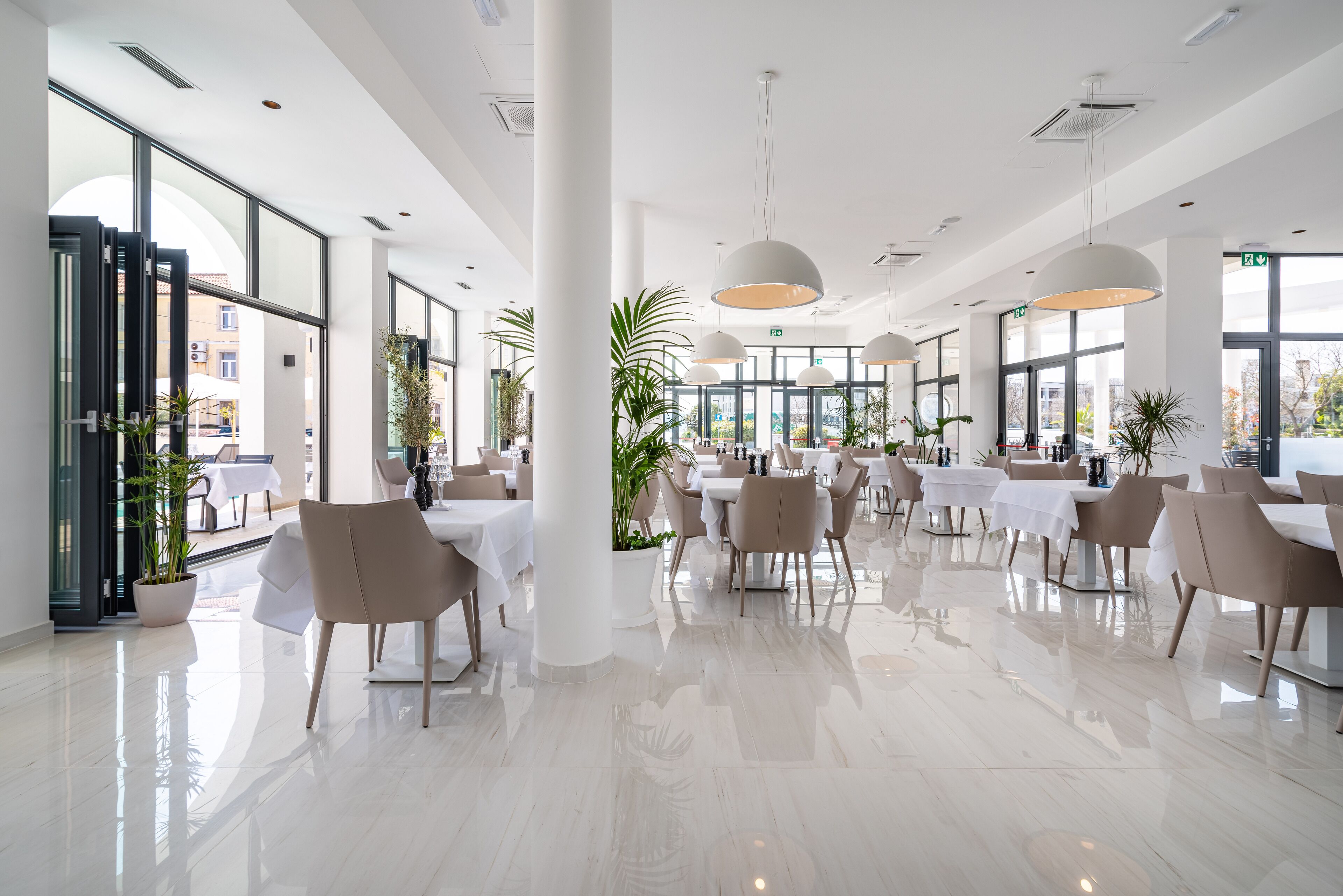 A spacious, modern dining area with large windows, white tables, and comfortable seating.