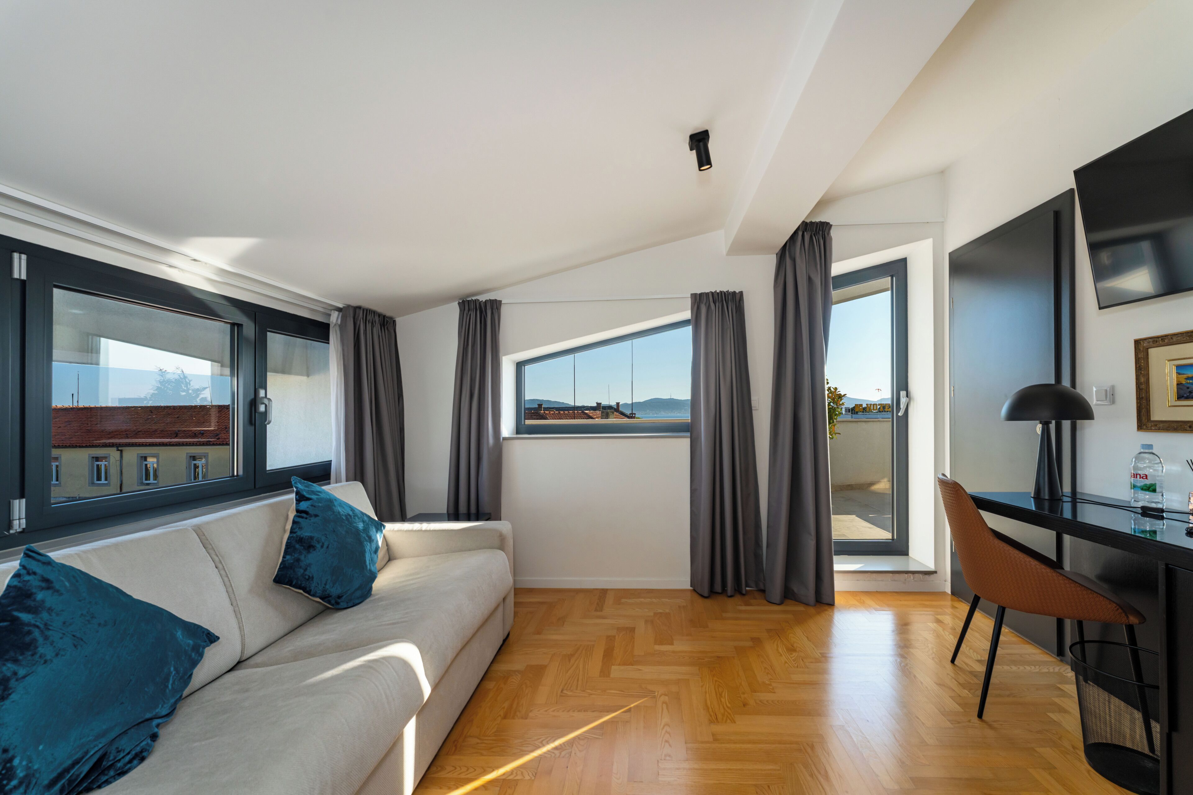 Un salon moderne comprenant un canapé, un coin repas avec une table et des chaises, une grande fenêtre offrant une belle vue et un téléviseur à écran plat fixé au mur.