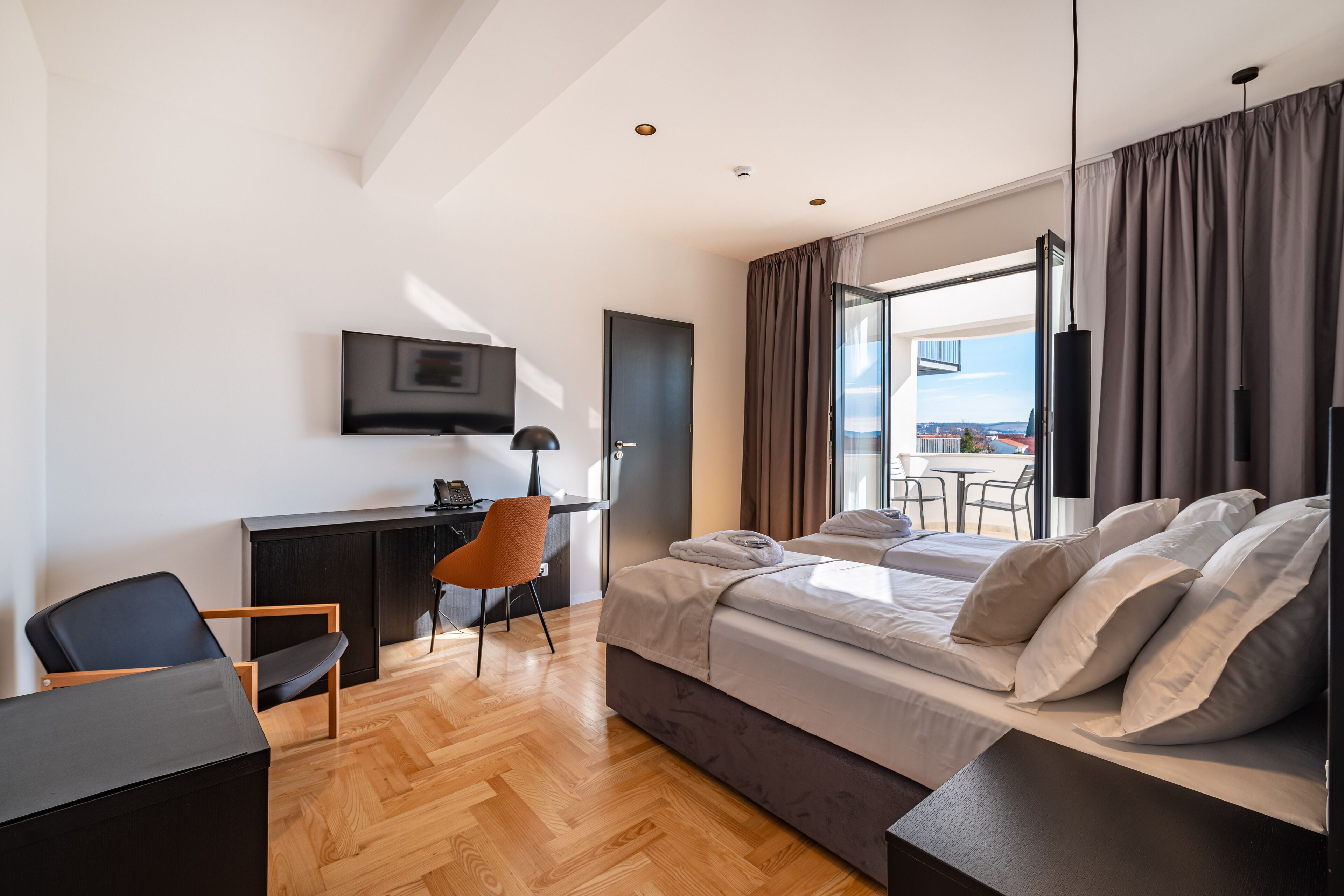 A modern hotel room with a bed, desk, chair, and a TV on the wall.
