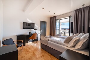 A modern hotel room with a bed, desk, chair, and a TV on the wall.