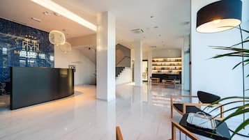 A modern hotel lobby with a reception desk, a staircase, and a seating area with a table and chairs.