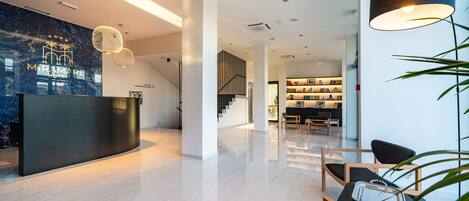 A modern hotel lobby with a reception desk, a staircase, and a seating area with a table and chairs.