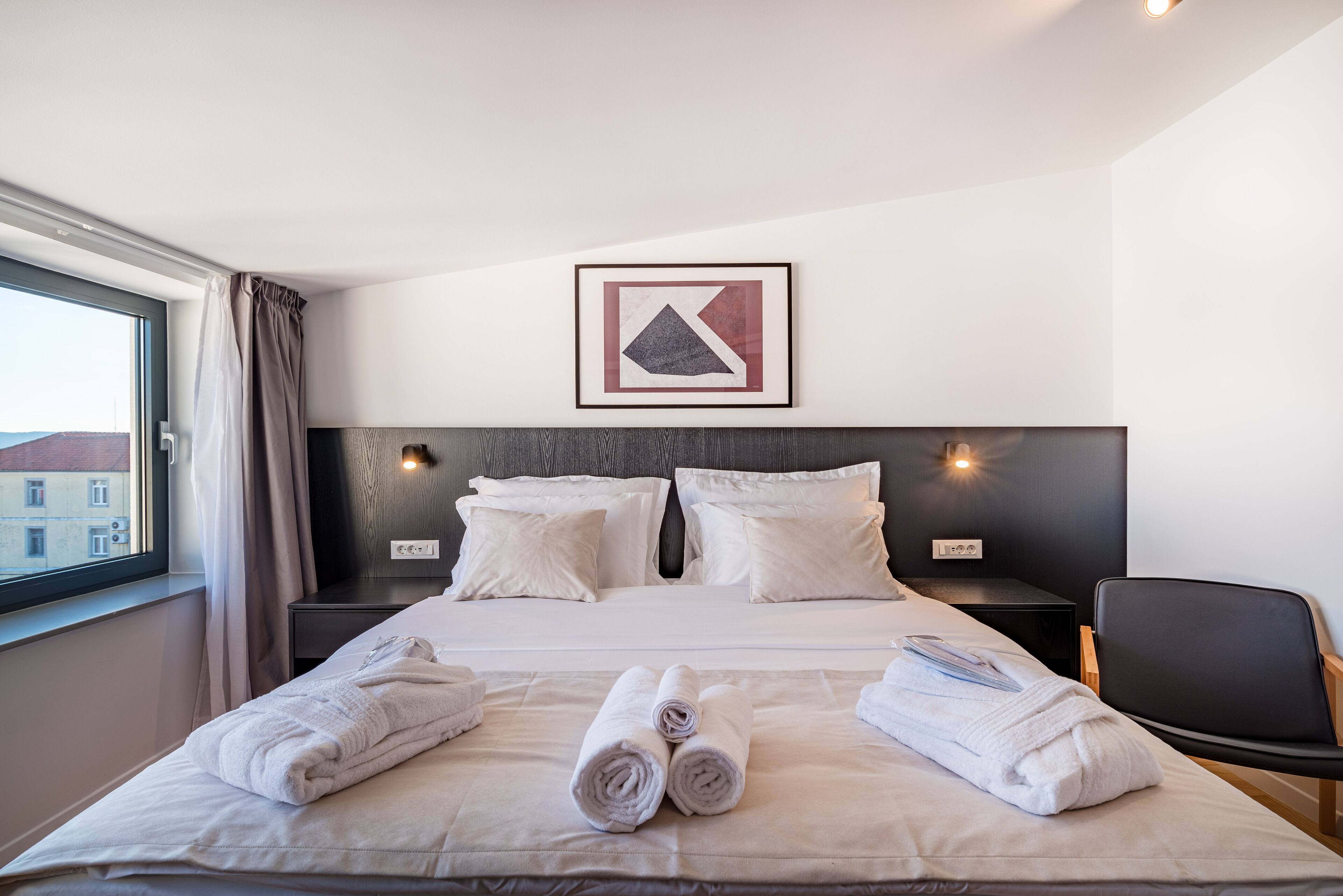 Une chambre d’hôtel avec un grand lit, deux tables de chevet, une chaise et une fenêtre avec des rideaux.