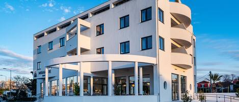 A modern hotel with a curved facade, multiple balconies, and a covered entrance area.