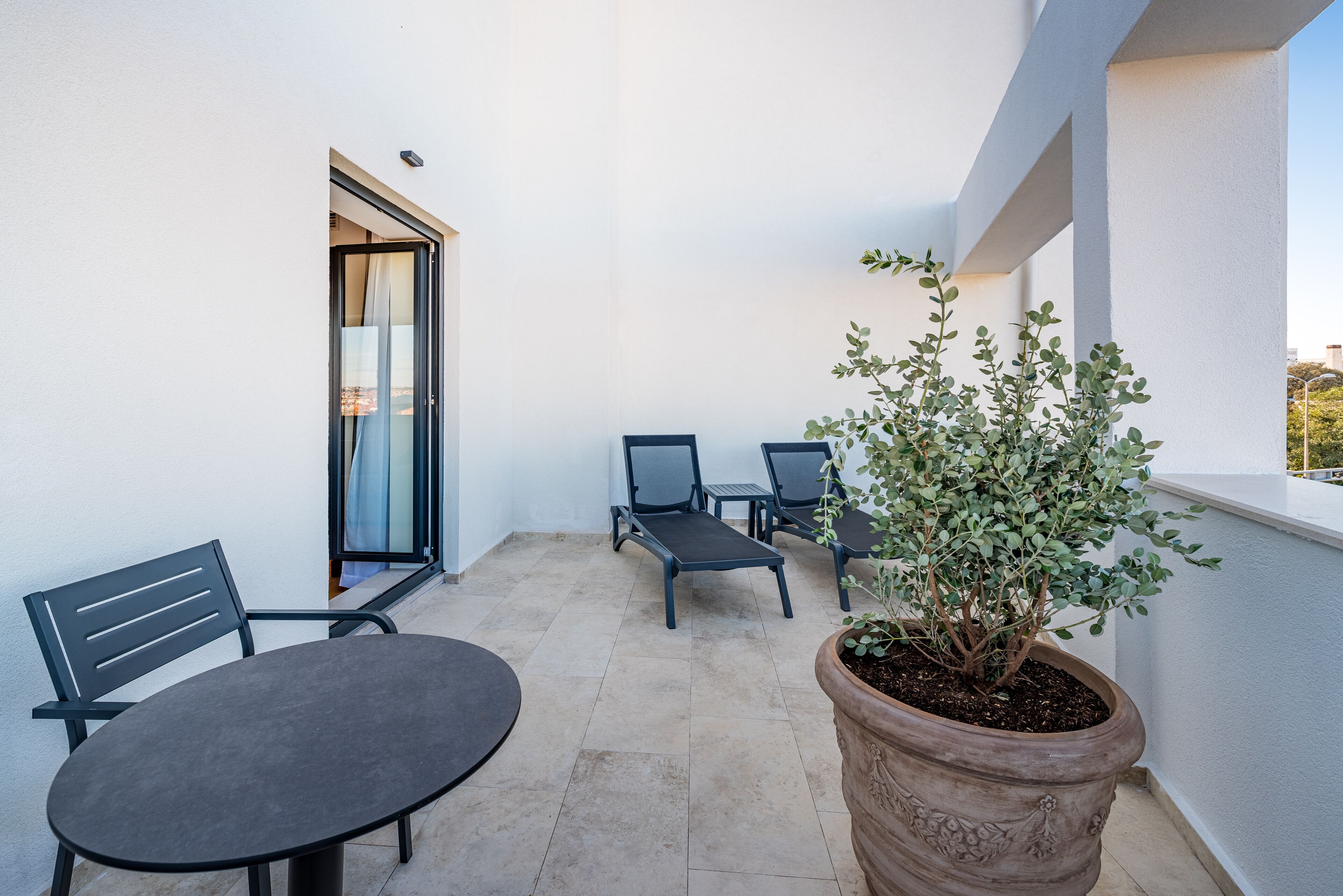 A balcony with a table and chairs, a potted plant, and a sliding glass door.