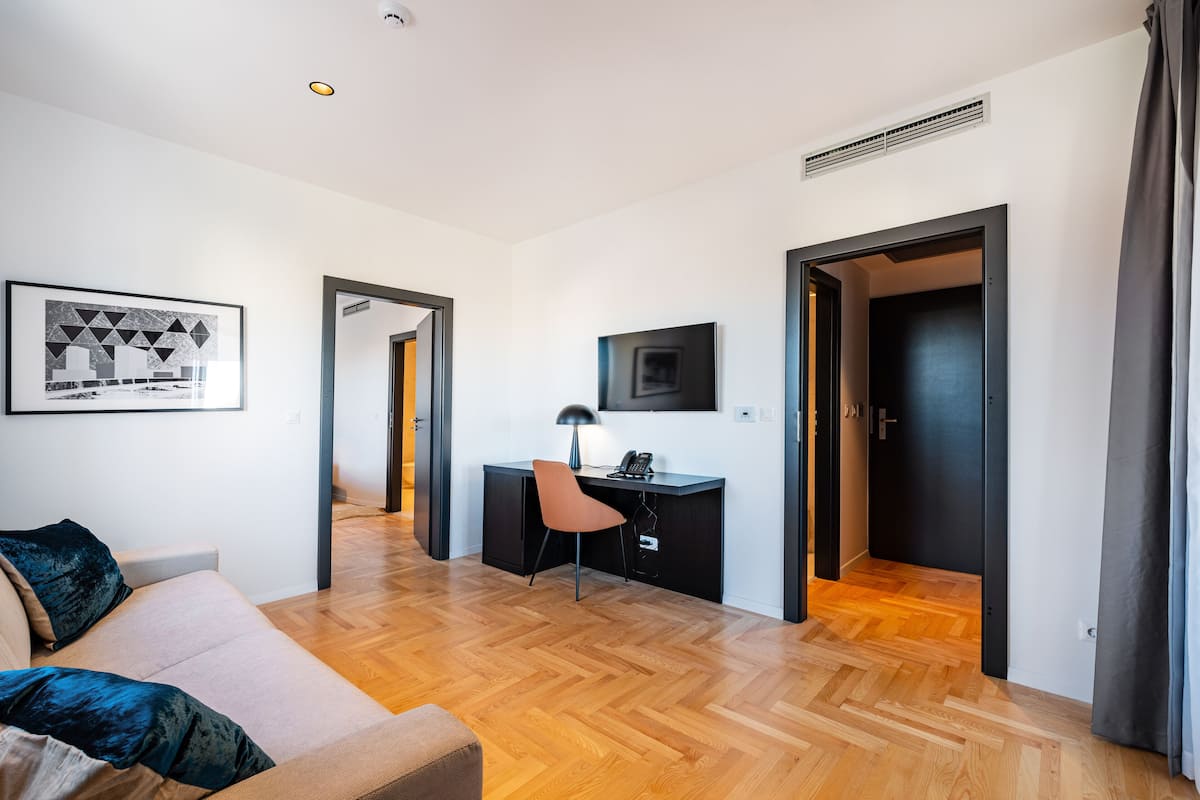 A modern living room with a sofa, a desk, and a chair. There are doors leading to other rooms.