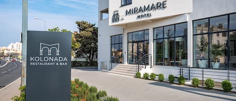 A modern hotel with a sign for Miramare Hotel and a restaurant named Kolonada.