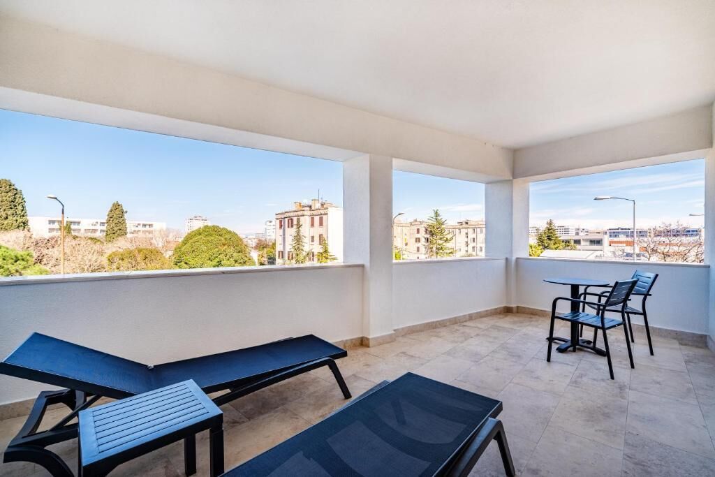 A balcony with a view of buildings and trees, a table with chairs, and a bench.