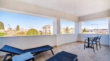 A balcony with a view of buildings and trees, a table with chairs, and a bench.