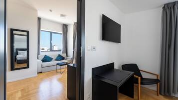 Een moderne woonkamer met een bank, een salontafel, een aan de muur bevestigde televisie en een fauteuil.