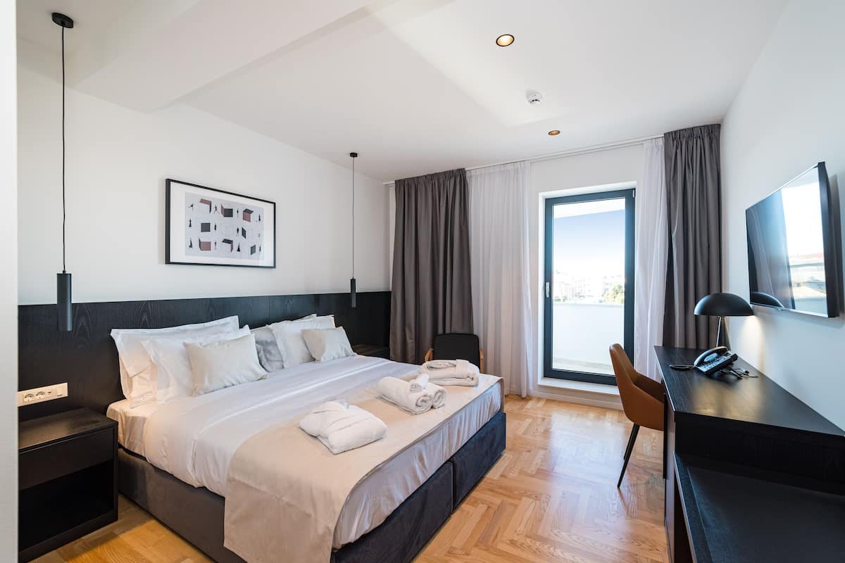 A modern hotel room with a large bed, a desk, and a view of the city.