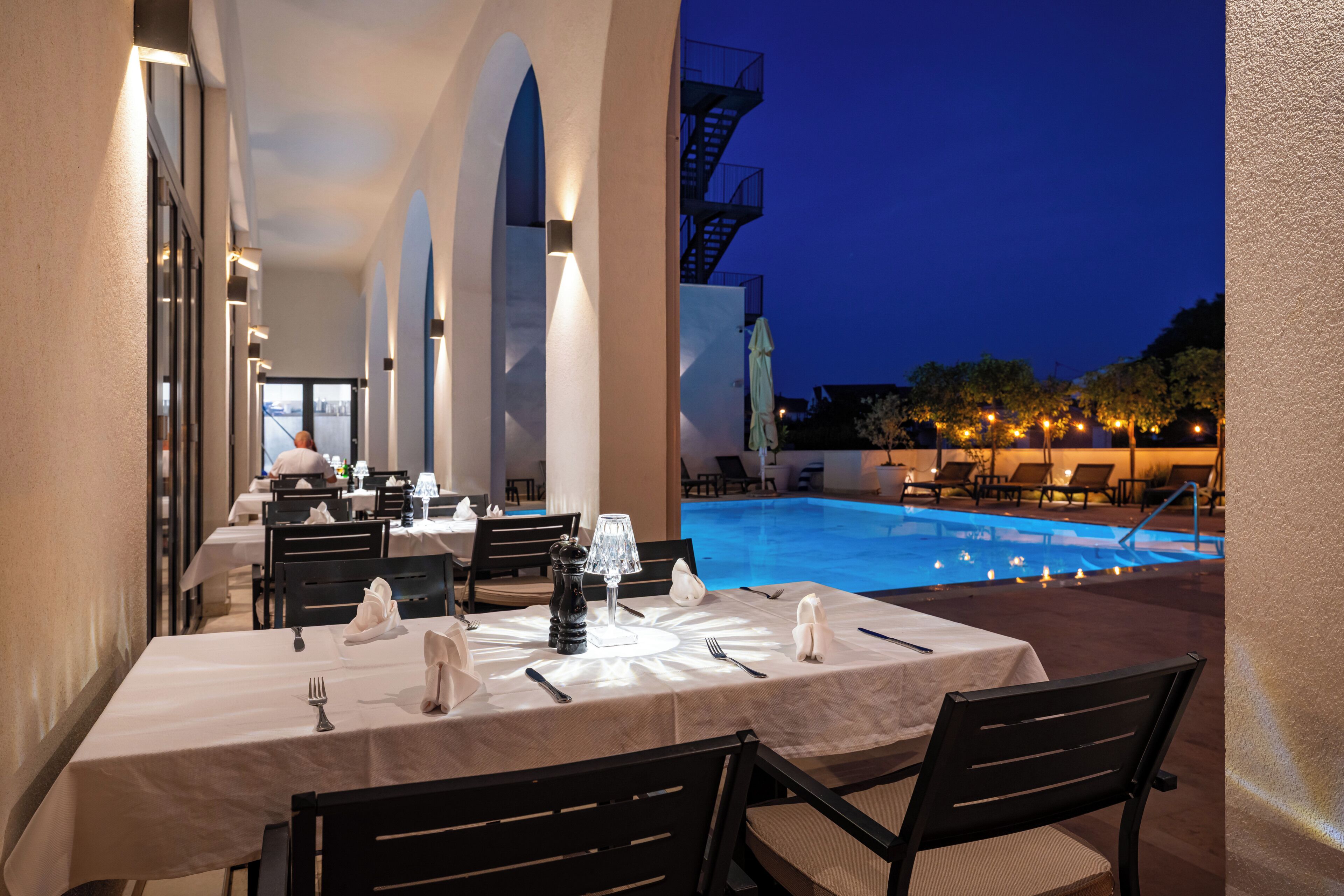 Un espace de restauration en plein air, avec des tables disposées pour deux personnes, donnant sur une piscine.