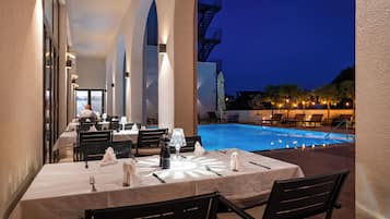 An outdoor dining area with tables set for two, overlooking a swimming pool.