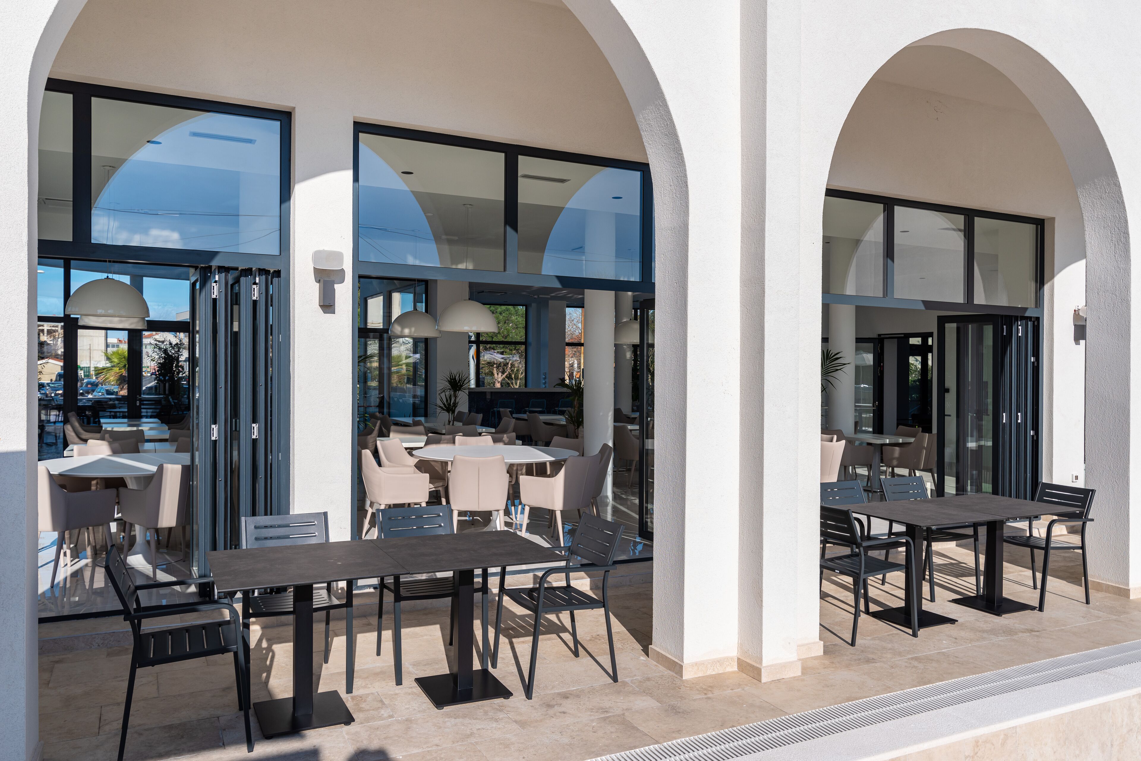 An outdoor patio area with tables and chairs, large glass doors, and a view of the city.