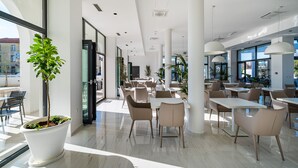 A modern indoor dining area with white tables and chairs, large windows, and potted plants. - Miramare Hotel Zadar (Zadar)