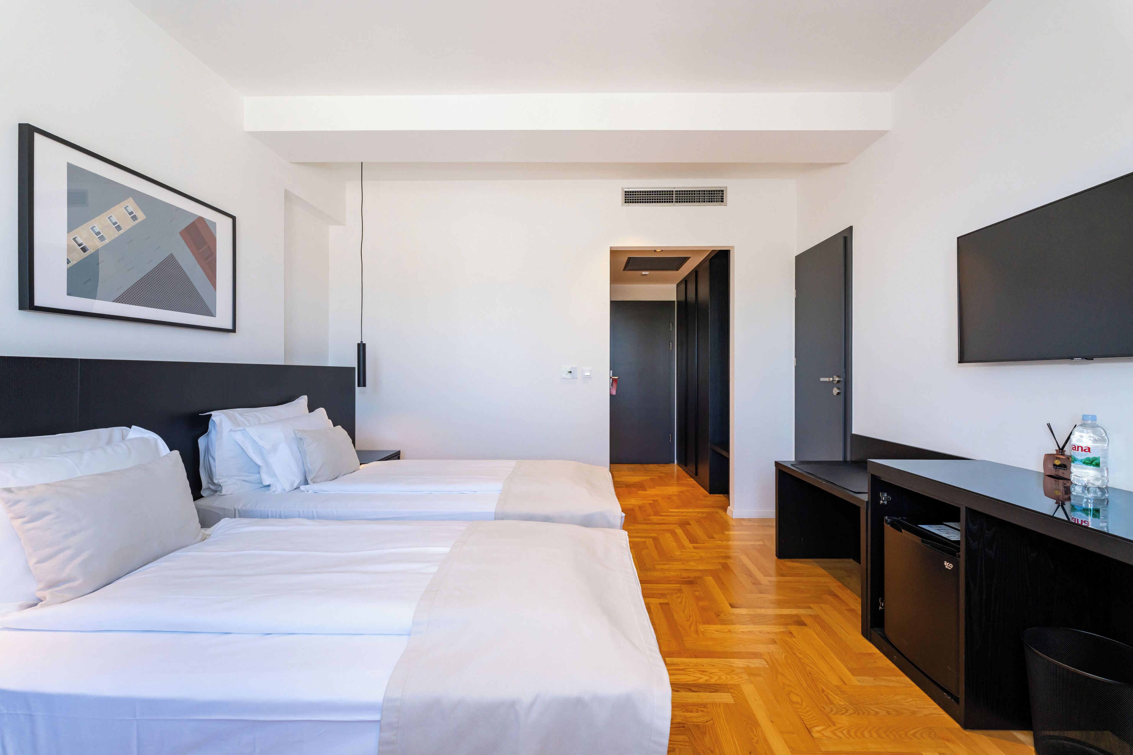 Habitación de hotel con dos camas, un escritorio, un televisor de pantalla plana y un cuadro en la pared.