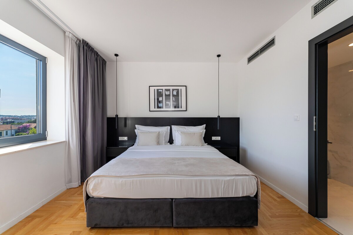 A modern bedroom with a large bed, a view of the city, and a black headboard.